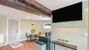 Eine moderne Küche mit Holzbalkendecke, einem Essbereich mit rundem Tisch und Stühlen sowie einem wandmontierten Fernseher.