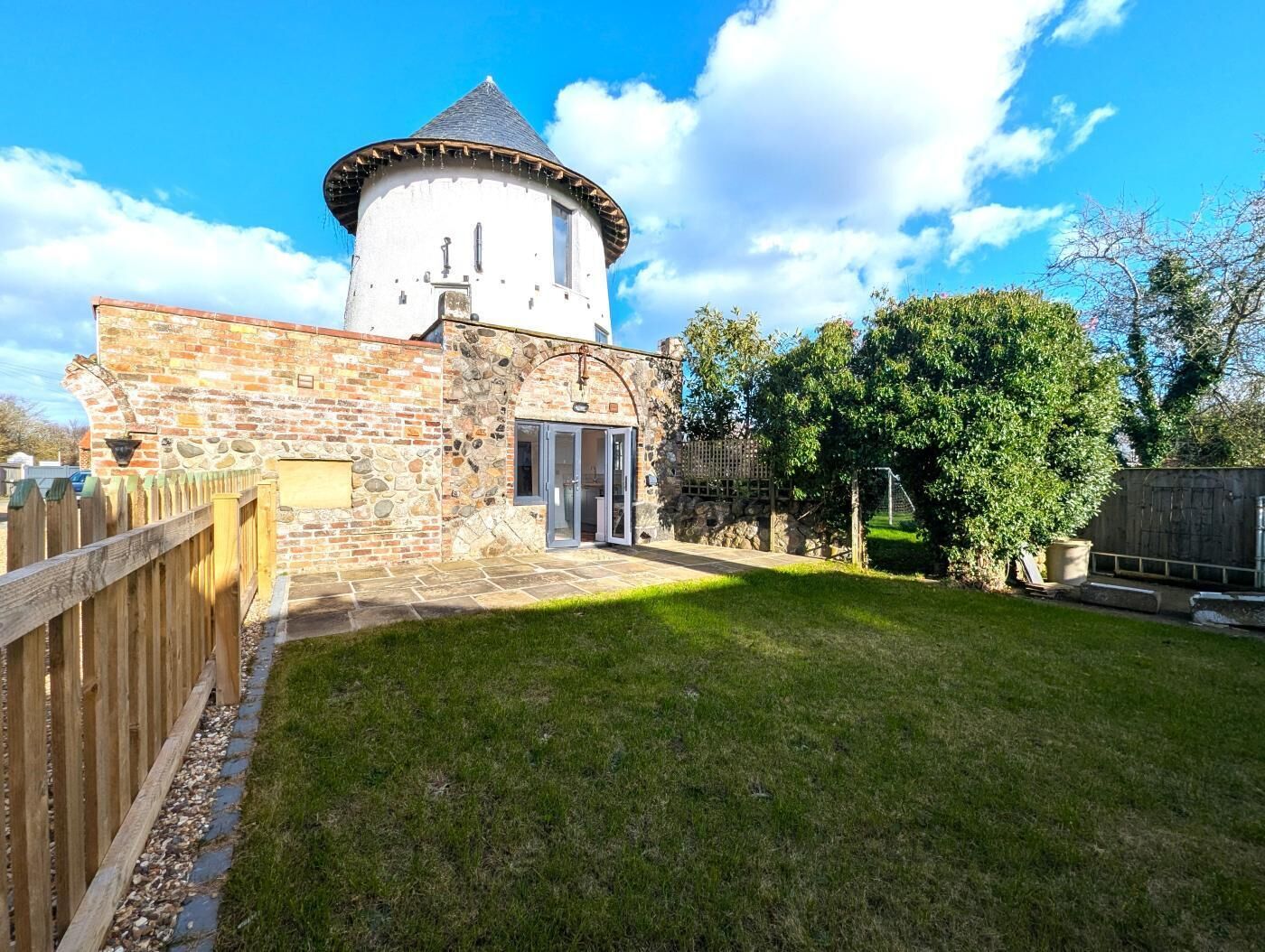 A stone building with a round tower, a wooden fence, and a grassy yard.