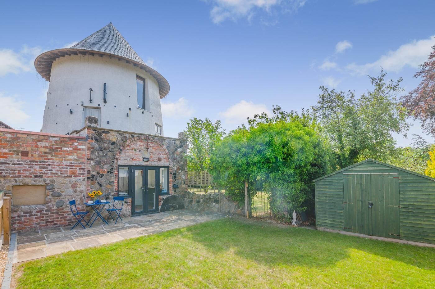 A white tower with a conical roof, a brick wall, and a green shed.