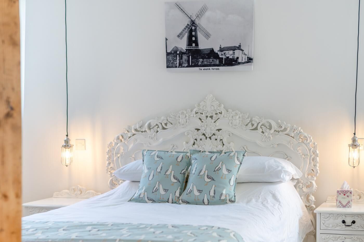 A bed with a white headboard, two pillows with seagull patterns, and a wall-mounted picture of a windmill.