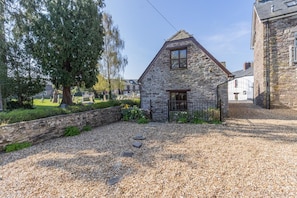 A stone building with a triangular roof, a gravel driveway, and a stone wall.