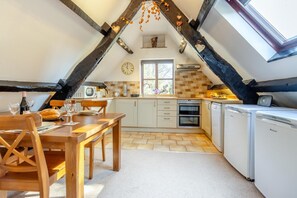 Une cuisine avec une table à manger, des chaises, une horloge et une fenêtre.