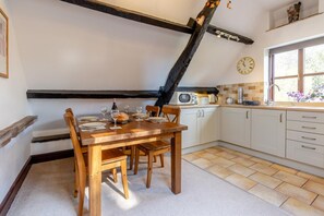 A dining area with a wooden table set for four, a kitchen with white cabinets, a microwave, and a clock on the wall. - 2 Bed in Llangorse (oc-p31754) (Llangorse)