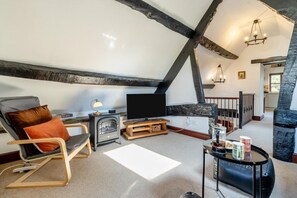 A loft-style room with exposed beams, a fireplace, a television, and a cozy seating area.