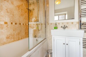 Une salle de bain avec une douche à parois de verre, un lavabo blanc avec un miroir au-dessus, et un mur recouvert de carreaux.