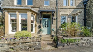 A stone house with a bay window, a green door, and a stone wall with flowers. - 4 Bed in Windermere (oc-o31130) (Windermere)
