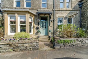A stone house with a bay window, a green door, and a stone wall with flowers. - 4 Bed in Windermere (oc-o31130) (Windermere)