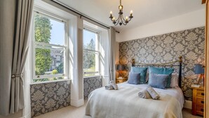 A bedroom with a large bed, two bedside tables, a chandelier, and a view of the outside. - 4 Bed in Windermere (oc-o31130) (Windermere)