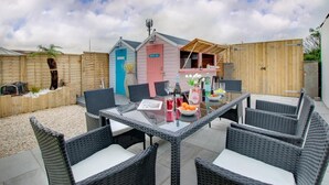 A patio area with a glass-top table surrounded by wicker chairs, a small pink and blue structure, and a wooden fence. - 3 Bed in Seahouses (oc-a25555) (Seahouses)