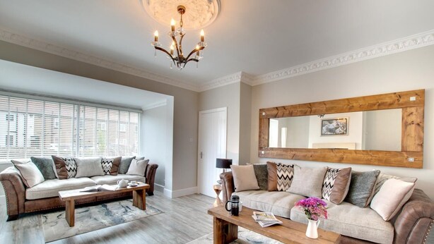 A living room with two sofas, a coffee table, a chandelier, and a large mirror. - 3 Bed in Seahouses (oc-a25555) (Seahouses)