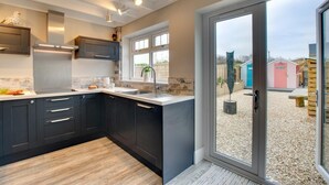 A modern kitchen with dark cabinets, a stainless steel range hood, and a large window. - 3 Bed in Seahouses (oc-a25555) (Seahouses)