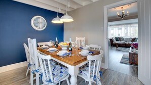 A dining area with a wooden table, white chairs, and a blue accent wall. - 3 Bed in Seahouses (oc-a25555) (Seahouses)