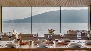 Ein Essbereich mit gedecktem Tisch, einer Couch und Blick auf einen See und Berge.