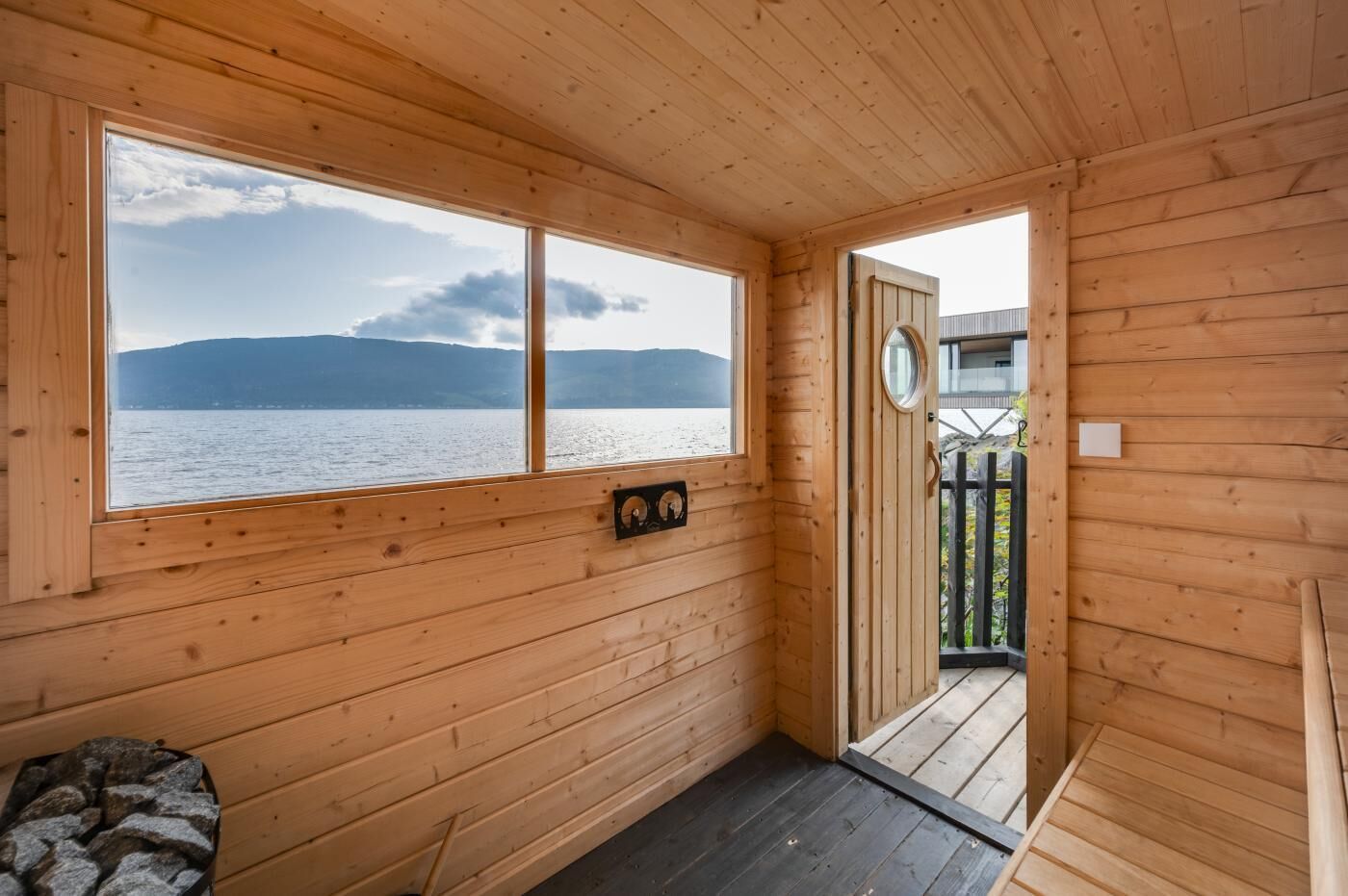 A wooden cabin with a large window overlooking a lake and mountains.