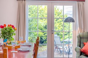 A dining area with a table set for two, a window with curtains, and a view of greenery outside. - 2 Bed in Dalmally (oc-m31803) (Cladich)