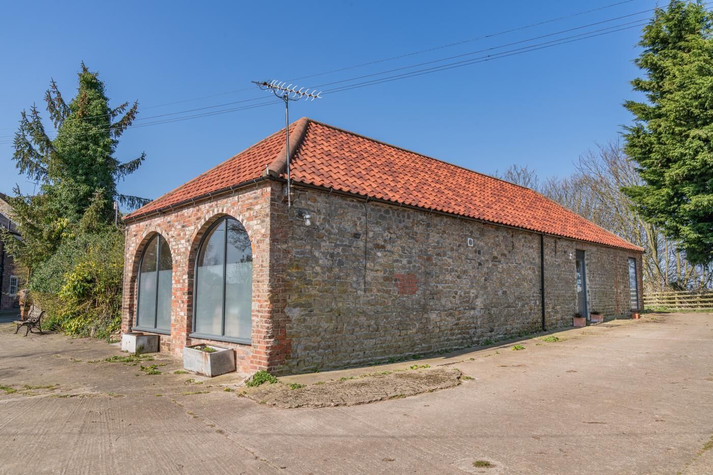 Un bâtiment en pierre avec un toit recouvert de tuiles rouges, des fenêtres en arc de cercle et une antenne métallique.