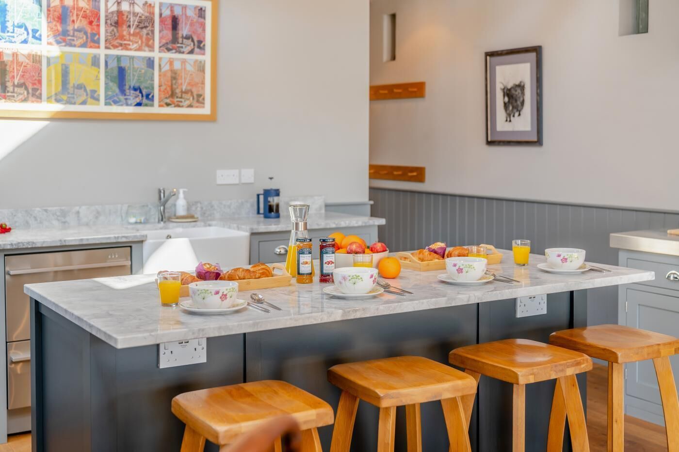 A modern kitchen with a marble countertop, wooden stools, and breakfast items.