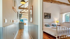 Un pasillo con vigas de madera, una cama con ropa de cama blanca y una ventana con vistas a árboles.