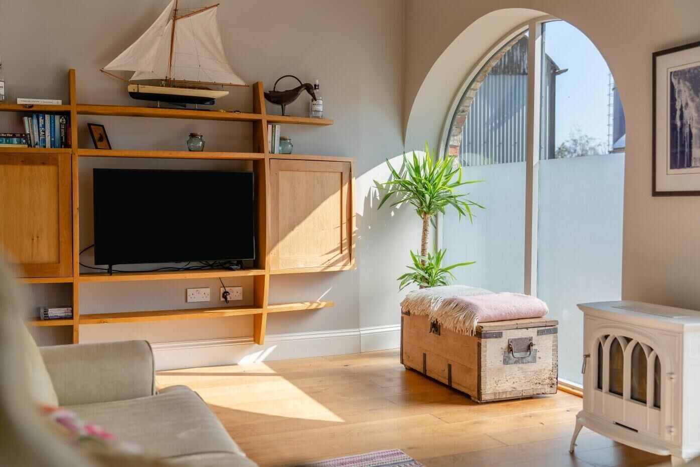 A living room with a wooden TV stand, a sailboat model, a small plant, and a vintage stove.