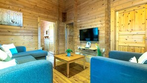 A wooden cabin interior with a TV mounted on the wall, a wooden coffee table, and two blue sofas.