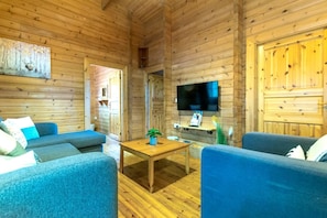 L’intérieur d’un chalet en bois, avec un téléviseur fixé au mur, une table basse en bois et deux canapés bleus.