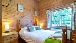 A wooden-paneled room with a bed, bedside lamps, a window with curtains, and a radiator.