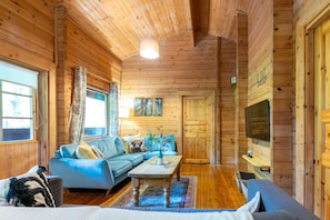 A wooden cabin interior with a sofa, a coffee table, a TV, and a window.
