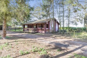 A rustic cabin with a porch, surrounded by trees and a fenced area.