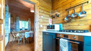 Puinen mökki sisältä, jossa on ruokailutila, keittiö ja näkymä avonaisesta ovesta.