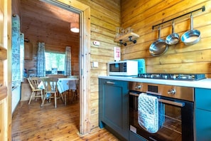 A wooden cabin interior with a dining area, kitchen, and a view through an open door.