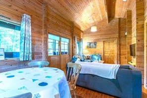 Interior de una cabaña de madera con una mesa de comedor, sofá y televisor.