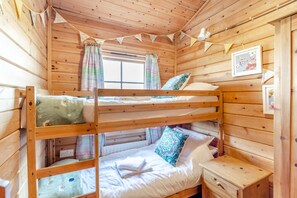 A bunk bed room with wooden walls, a window, curtains, a bedside table, and a framed picture on the wall.