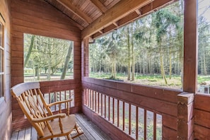A wooden porch with a wooden chair, a railing, and a view of a forest.