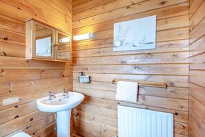 A wooden-paneled bathroom with a white sink, mirror, towel rack, and a framed picture on the wall.