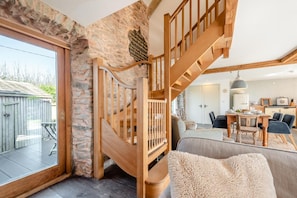 A spacious living area with a wooden staircase, stone wall, and a view of a backyard.