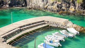 A marina with boats docked at a curved concrete pier surrounded by clear turquoise water and rocky cliffs. - 2 Bed in St. Davids (oc-t31868) (St Davids)
