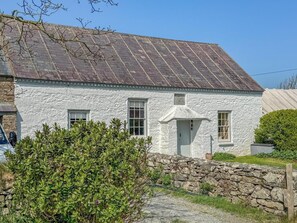 A white cottage with a stone wall and a metal roof.