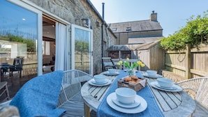 An outdoor dining area with a stone wall, a wooden table set with plates, bowls, and a basket of bread. - 2 Bed in St. Davids (oc-t31868) (St Davids)