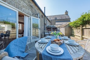 An outdoor dining area with a stone wall, a wooden table set with plates, bowls, and a basket of bread.