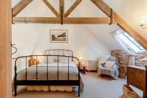 A bedroom with a sloped ceiling, a bed, a chair, a table, a lamp, and a picture on the wall.