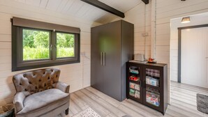A room with a tufted armchair, a dark cabinet with glass doors, a window with a view of greenery, and a door with a light fixture. - 1 Bed in Wilmington (oc-l31867) (Wilmington)
