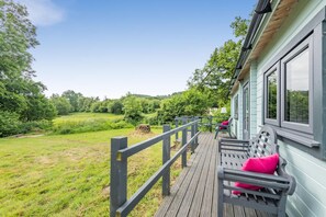 Eine Holzterrasse mit einer Bank, einer Laterne und Blick auf eine grüne Landschaft.