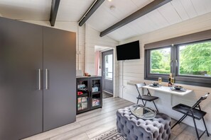 A modern kitchen with a dining area, a grey wardrobe, a built-in TV, and a window with a view of greenery.