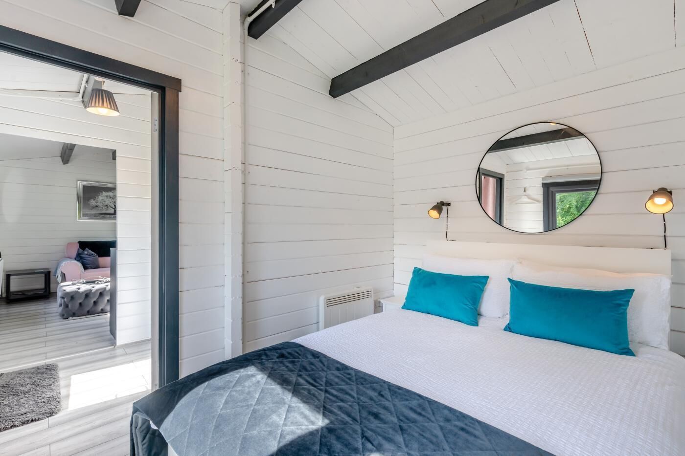 Une chambre avec un lit, un miroir rond et une vue sur une autre pièce.