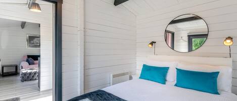 Une chambre avec un lit, un miroir rond et une vue sur une autre pièce.