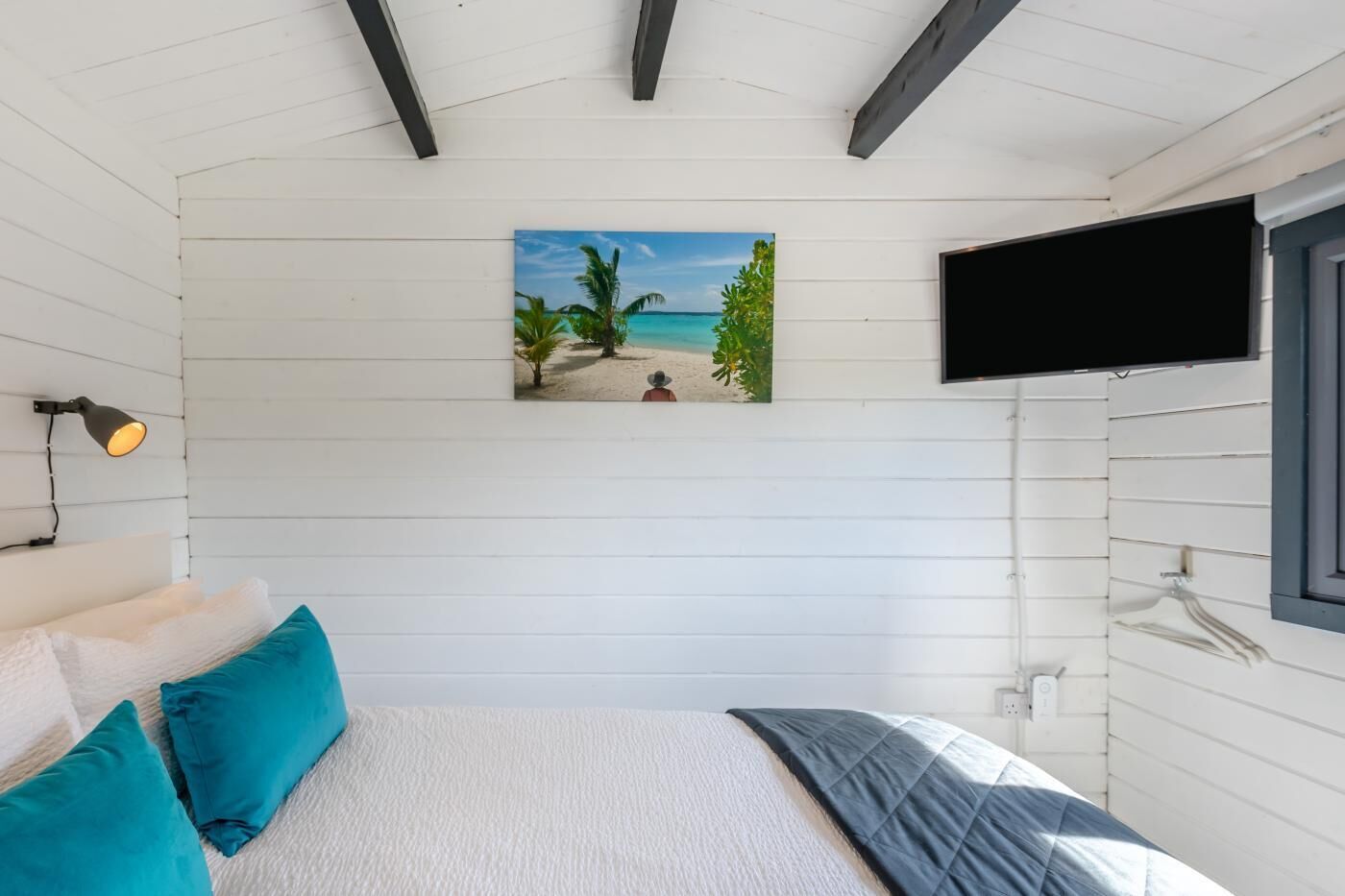 Une chambre à coucher avec un lit, un tableau représentant une plage, une télévision et une lampe.