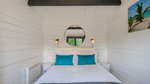 A bedroom with a bed, two bedside lamps, a round mirror, and a beach-themed wall art. - 1 Bed in Wilmington (oc-l31867) (Wilmington)