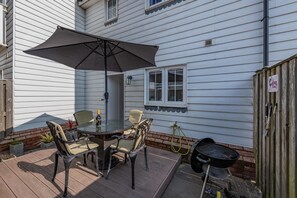 Eine Terrasse mit einem runden Tisch, Stühlen und einem großen Sonnenschirm.