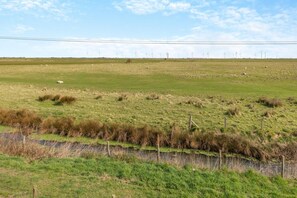 A rural landscape with a grassy field, a fence, and wind turbines in the distance. - 2 Bed in Camber (oc-r31753) (Camber)