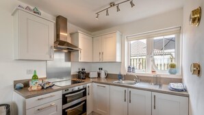 A modern kitchen with white cabinets, a stainless steel range hood, a built-in oven, and a window with a view of a building outside. - 2 Bed in Camber (oc-r31753) (Camber)